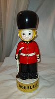 Front view of the vintage Beefeater decanter, showing the soldier figure with red coat, white belt, black boots, and large black hat. The base has the word 'DOUBLE!!' printed on it.