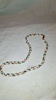 Full view of the entire twisted multi-strand gemstone necklace laid out on a fabric background, showing the overall length and strand design.