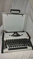 Front view of Olympia Traveller De Luxe typewriter in open case on white fabric background.