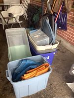 Photo showing stacked plastic storage bins of various sizes with some lids, with tarps stored inside the front gray bin.