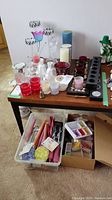Overview of various candles and candle holders arranged on a table including a storage bin with assorted taper candles and a box of assorted small candles.