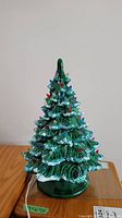 Front view of green ceramic Christmas tree with multicolored attached lights on a wooden surface.