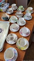 Multiple tea cups and saucers with varied floral patterns arranged on wooden table to show the collection.