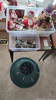 Two plastic bins filled with various Christmas decorations including Santa and snowman soap dispensers, mouse and snowman figurines, cheese cutters with Christmas-themed handles, and angel candle holder. Also includes two candles and horse-drawn carriage snow figurines.