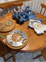 View of entire lot showing two clocks, barometer and blue miniature kitchen knickknack on round wooden table