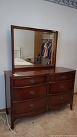 Front view of solid wood dresser with attached mirror showing six drawers with brass color hardware and curved front design.