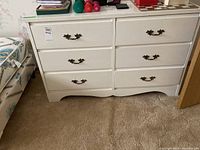 Front view of the white dresser with six drawers and ornate handles, showing overall condition and finish.