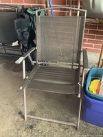 Close-up of dark resin mesh and metal frame lawn chair with minor surface rust, showing foldable design and armrests.