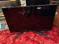 Front view of LG TV on red carpet with remote at base