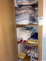 Shelves with neatly folded assorted linens including sheets, pillow cases, and tablecloths in various neutral colors.