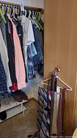 Closet with men's shirts, pants, some shoes on rack, and a rack holding multiple ties and belts.