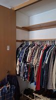 Closet view showing a row of men's shirts on hangers, many plaid patterns, various colors, sizes medium and large.
