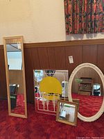 Four mirrors set up on red carpet against wooden wall paneling, showing variety of frames and sizes