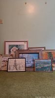 Group shot showing seven assorted framed and matted prints leaning against wall on carpeted floor.