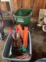 Scotts Basic broadcast spreader with green hopper labeled 'Scotts Basic'. Surrounding area and tools in gray plastic bin visible.