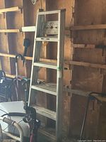 Full view of the aluminium step ladder leaning against wooden wall with some tools nearby.