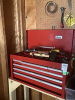 Front view of red metal Beach brand tool box with 6 drawers closed, placed on wooden stand against wall.