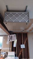 Grey rectangular metal air filtration unit mounted to ceiling with front pleated filter visible