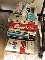 Photo of stacked vintage board games showing Flinch, Pente, Uno Rummy-Up, Monopoly Seattle Edition, Monopoly Las Vegas Edition and others.