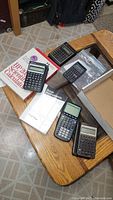 View of all five calculators on a wooden table along with manuals and box for the HP calculator.