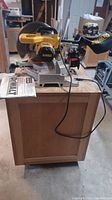 Full view of the DeWalt miter saw mounted on wooden cabinet with manual on table, power cord visible