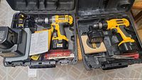 Two Dewalt cordless drills pictured in open black plastic carrying cases with batteries, chargers, bits and manuals.