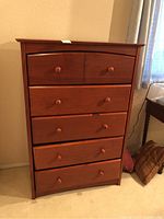 Front view of the tall wood dresser showing five drawers with two knobs each, some damage visible on the lower drawers.