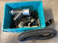 Top view of blue container with assorted dust collection fittings, casters, and wood pieces inside, with flexible hose draped outside container.