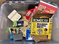Plastic bin with assorted electrical parts including wire rolls, outlet boxes, and switches.