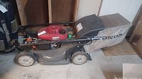 Side view of Honda gas lawn mower showing deck, wheels, engine housing, and bag attached