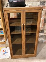 Front view of Sonrise wooden media cabinet with glass paneled double doors and wooden handles. Visible interior shelves are empty.