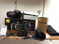 All items displayed on shelf: D60 kit box, camera with 18-55 lens, telephoto lens in box, charger, cables, strap and pouch