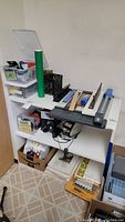 Office supplies stored on white shelving including paper cutter, tape, scissors, labels, and rulers.