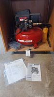 Porter-Cable pancake compressor model CF2600 on wooden rolling platform with pressure gauges and regulator, small black case, and original manuals placed on floor.