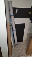 Rolls of paper and large black foam boards standing upright on a tiled floor.