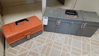 Two closed tool boxes on floor: one orange Tough Box and one gray metal Holley box