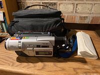Sony DCR-TRV320 Digital8 Handycam video camera with carrying case and accessories arranged on a wooden table against a brick wall background.