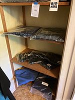 Shelf containing various men's clothing items including jeans, dark shirts or pants, and blue chinos on bottom shelf.