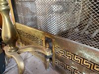 Close-up of the brass fireplace screen showing the Greek key border and mesh screen.