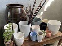 Photo of the entire assortment of ceramic pots, glass vases, small planters with succulents, and decorative sticks on and around a wooden rack and metal filing cabinet.