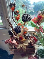 Tall floral arrangement with orange flowers, lotus seed pods and twigs in wooden base, view from side