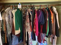 Large rack of women's clothing hung on a wooden rod, showing a variety of colors and types including sweaters, tops, and jackets.