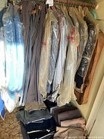 Men's suits and slacks hanging on rack with many jackets in plastic bags and slacks folded below