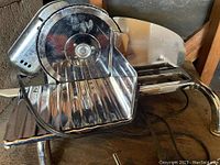 Front angle showing slicer with chrome finish, blade, groove tray, and adjustable food holder.