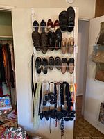 Two white metal over-the-door shoe racks loaded with men's and women's shoes including black and brown casual shoes, sandals, and sports shoes.