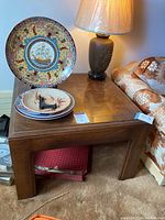 Wood end table with lamp and decorative plates on top, showing wood grain and square legs.