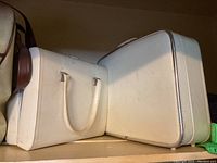 Photo showing two white hard-sided luggage pieces and a white tote bag on a shelf