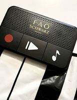 Close-up of the FAO Schwarz logo and three control buttons on the black plastic control panel (red circle, play, music note).