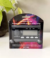 Front of Seiko SAT100 Guitar and Bass Tuner in sealed packaging showing product name, screen, buttons, and colorful background.