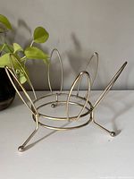 Front angle view showing brass-toned wire design with oval vertical supports and three legs with ball feet.